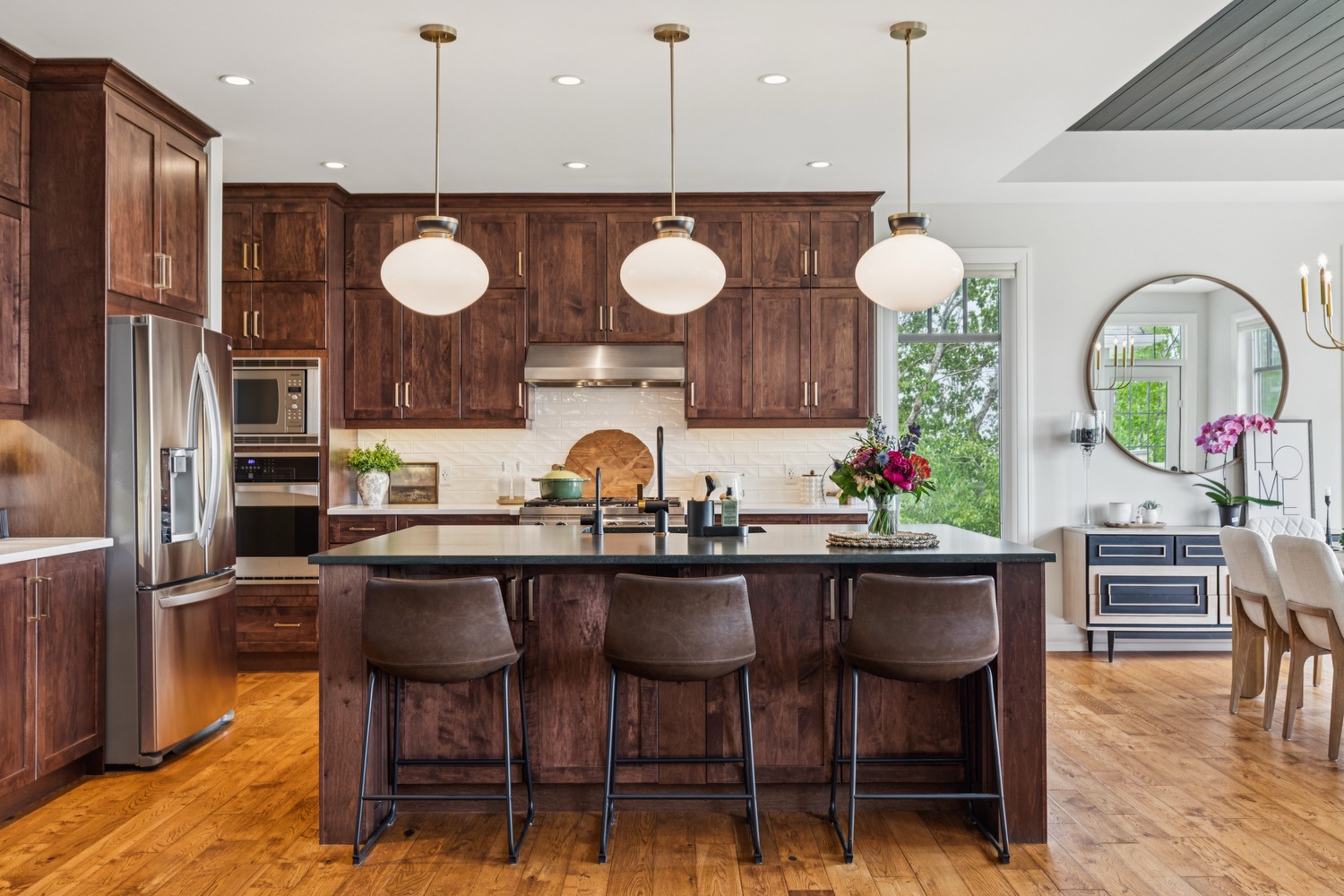 Kitchen with dark wood cabinets, stainless refrigerator, and a large island under three pendant lights.